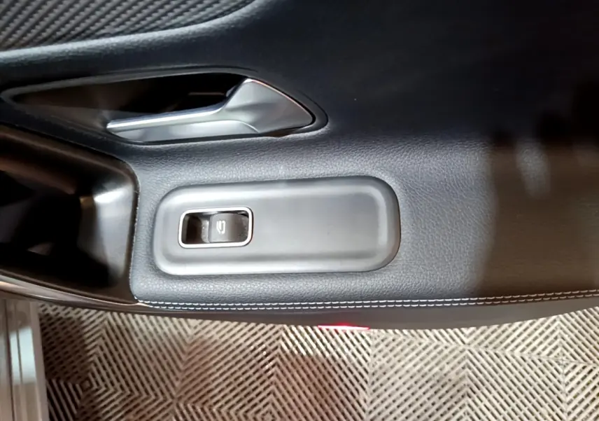 Gros plan sur la commande de lève-vitre et poignée intérieure en cuir noir sur la porte côté conducteur d'une Mercedes CLA 180 d gris clair.