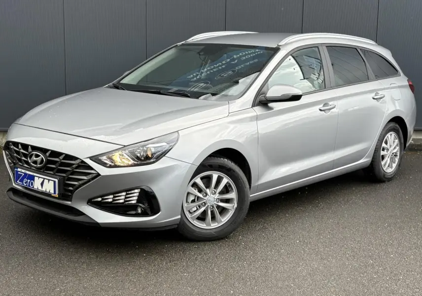 Hyundai i30 SW gris argent vue 3/4 avant droit, avec jantes alliage et projecteurs allumés.