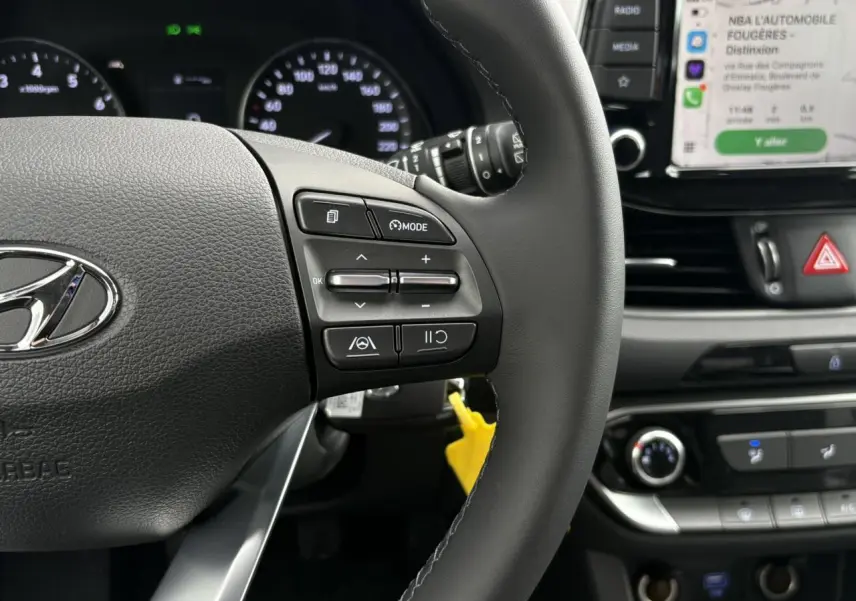 Gros plan sur le volant cuir gris et tableau de bord d’une Hyundai i30 SW 2025 avec écran tactile Apple Car Play visible.