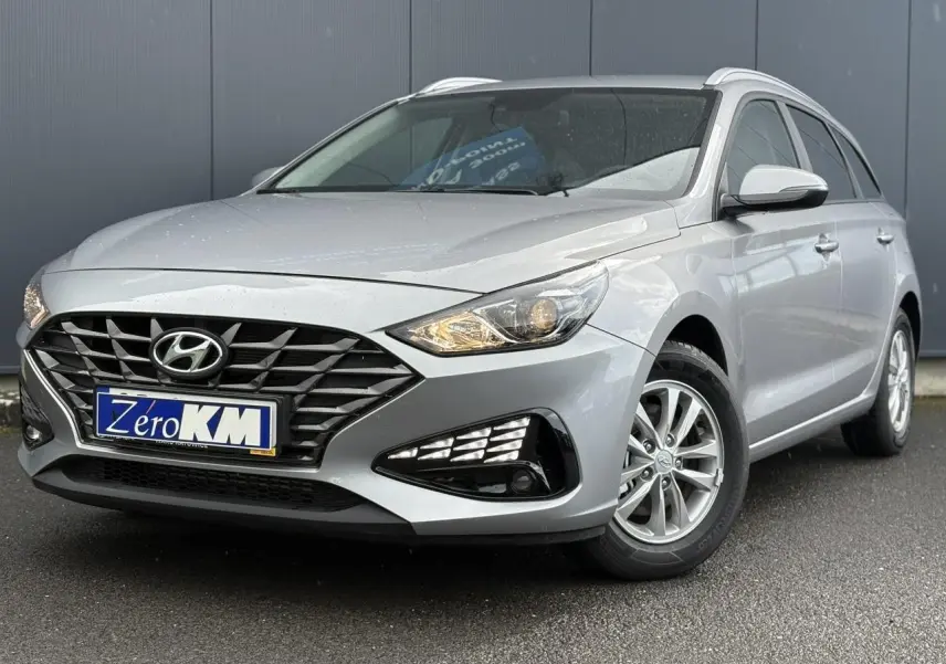 Hyundai i30 SW gris argent vue 3/4 avant droit, avec calandre noire et jantes alliage visibles.