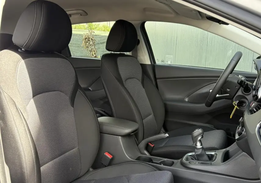 Vue intérieure côté droit montrant les sièges avant noirs et gris, accoudoir coulissant et levier de vitesses cuir de la Hyundai i30 SW 2025.