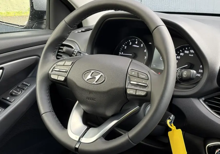 Vue rapprochée du volant cuir noir de la Hyundai i30 2025, avec commandes intégrées et tableau de bord visible.