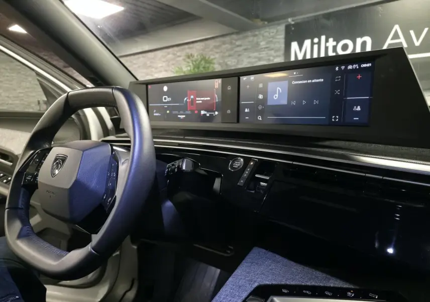 Vue intérieure côté conducteur du Peugeot 5008 blanc 2025, avec volant compact et double écran panoramique HD flottant.