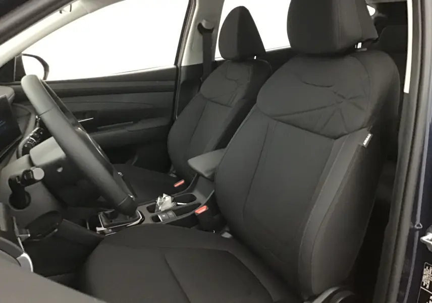 Vue intérieure côté conducteur du Hyundai Tucson 2025 bleu Salling, sièges avant en tissu noir avec volant cuir.
