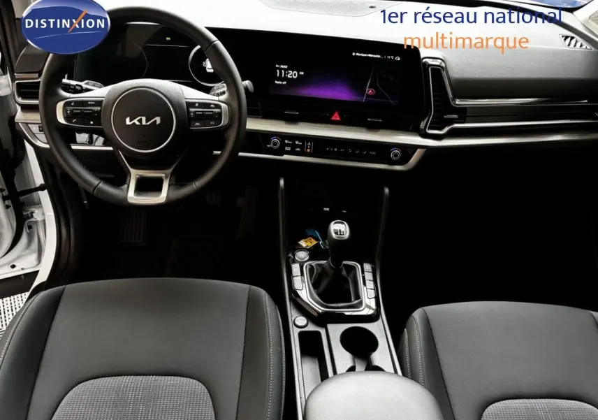 Vue intérieure frontale du tableau de bord et volant noir du Kia Sportage blanc nacré 2025 avec boîte manuelle.