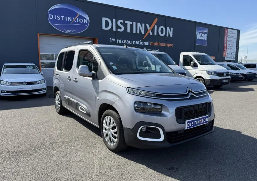 Vue 3/4 avant d'un Citroën Berlingo gris foncé garé devant un concessionnaire Distinxion par temps clair.
