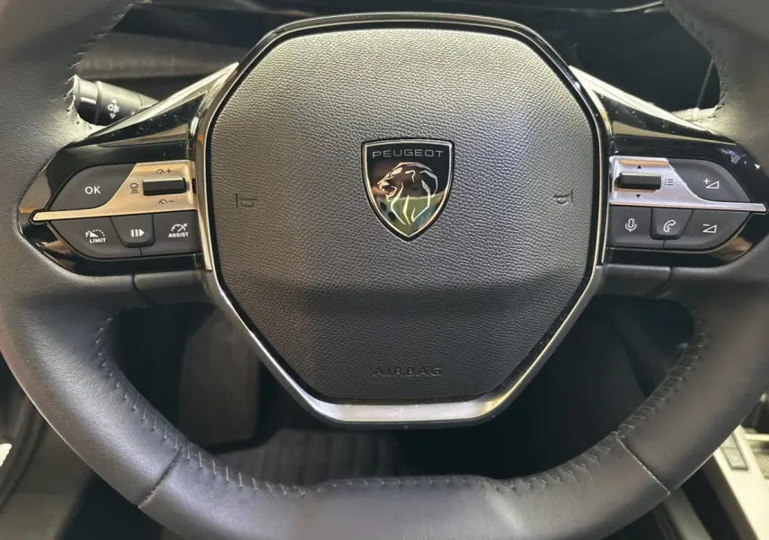 Gros plan sur le volant cuir noir de la Peugeot 308 2024 avec commandes multifonctions intégrées et logo central.