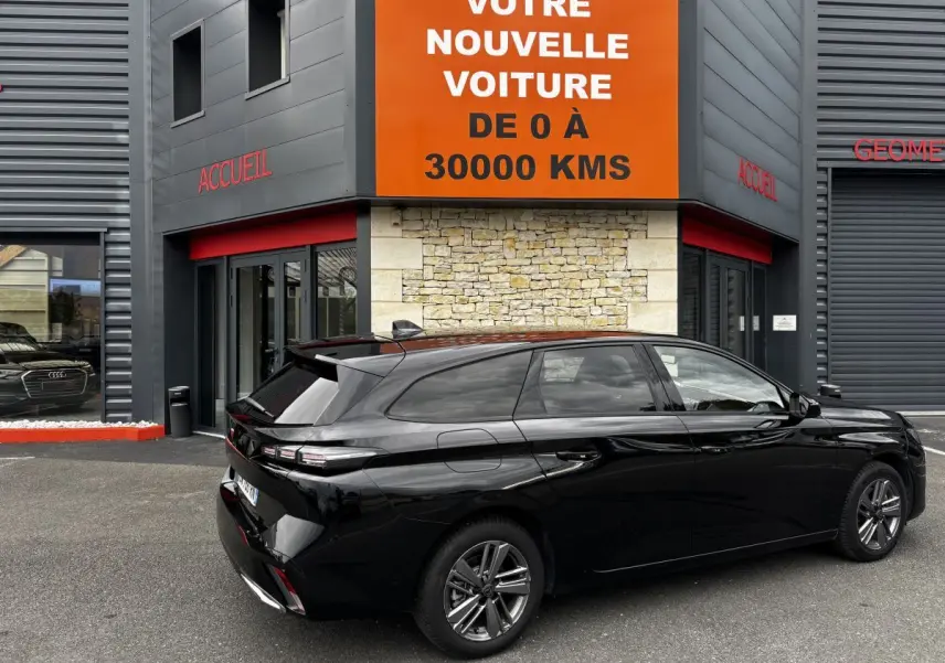 Peugeot 308 PureTech 130 noire vue de trois quarts arrière droit, stationnée devant un bâtiment moderne.