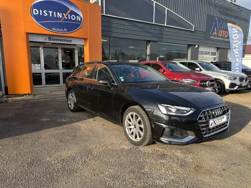 Audi A4 Avant noir brillant vue en 3/4 avant droit, stationnée devant un concessionnaire avec d'autres voitures visibles.