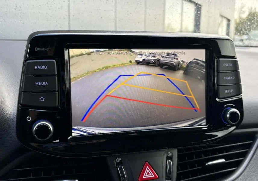 Écran tactile central de la Hyundai i30 SW 2025 montrant la caméra de recul avec lignes de guidage colorées.