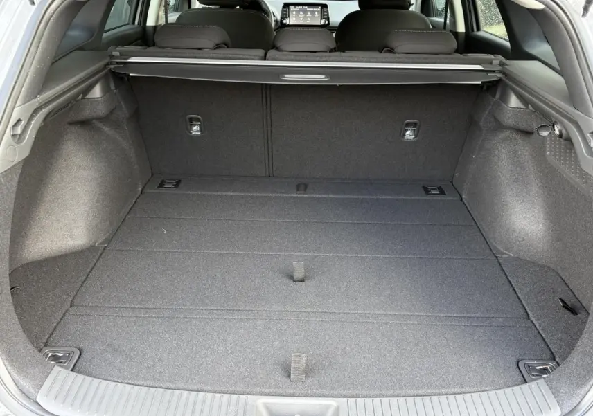 Coffre spacieux ouvert vu de l'arrière d'une Hyundai i30 SW gris argent, avec cache-bagages et sièges rabattus.