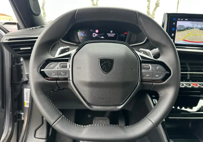 Vue rapprochée du volant cuir noir du Peugeot 2008 Hybrid 136 e-DCS6 Allure avec commandes intégrées et écran tactile visible.