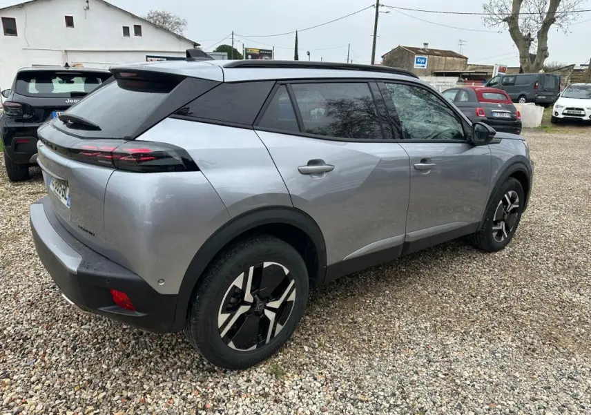 Peugeot 2008 Hybrid gris en 3/4 arrière droit, avec barres de toit et jantes alliage 17 pouces visibles.