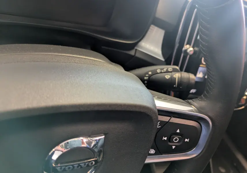 Gros plan sur le volant noir du Volvo XC40 marron clair, avec commandes intégrées et levier d'essuie-glace visible.