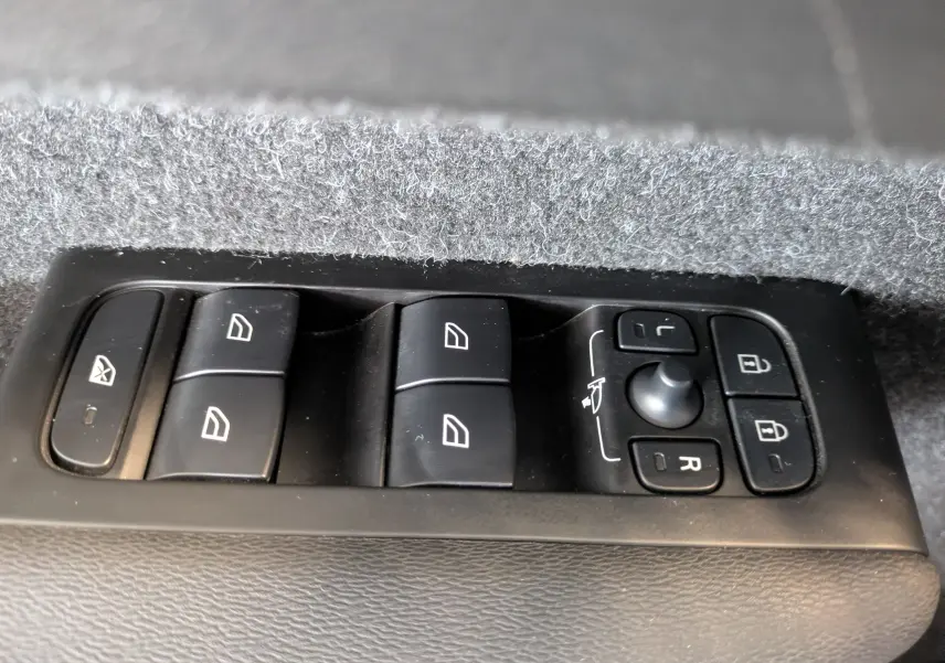 Gros plan sur les commandes de lève-vitres et réglage des rétroviseurs du Volvo XC40 Momentum marron clair.