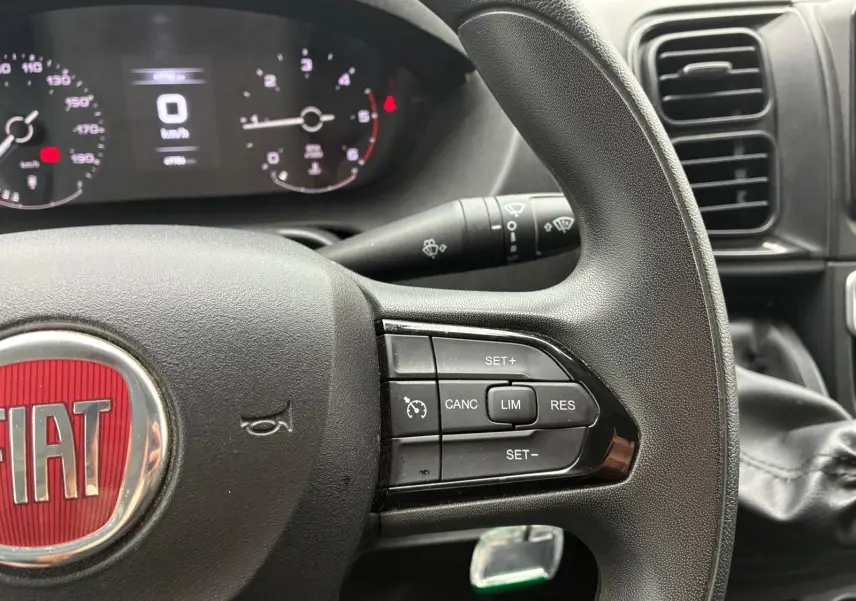 Gros plan sur le volant noir du Fiat Ducato Fourgon 2023 avec commandes de régulateur de vitesse et tableau de bord numérique.