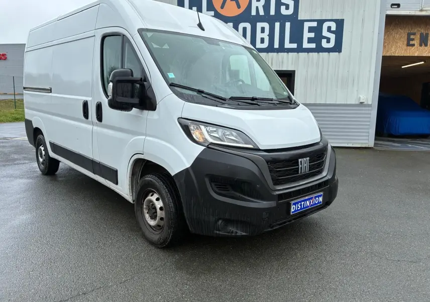 Fiat Ducato Fourgon blanc en 3/4 avant droit, avec pare-chocs noir et plaque Distinxion visible.