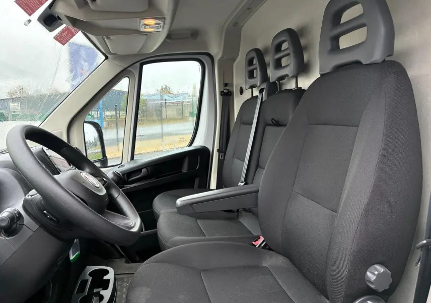 Vue intérieure côté conducteur du Fiat Ducato Fourgon blanc 2023, montrant les sièges noirs et le volant.