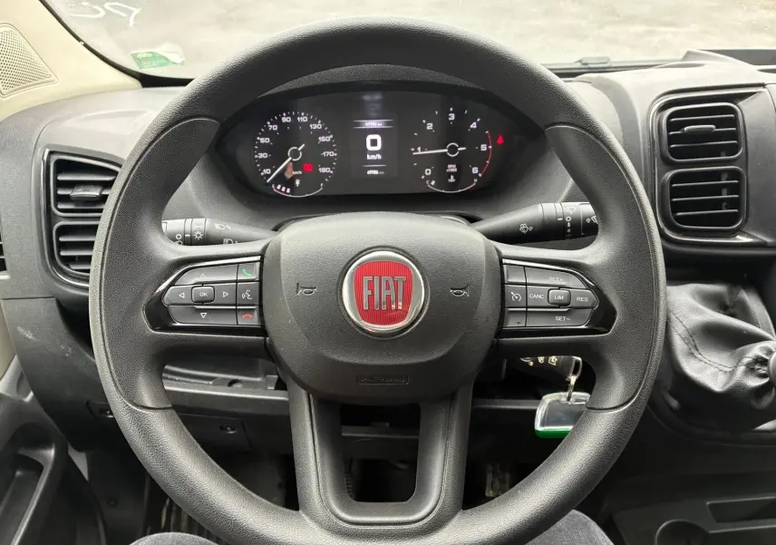 Vue intérieure centrée sur le volant noir du Fiat Ducato Fourgon 2023 avec tableau de bord et levier de vitesses visible à droite.