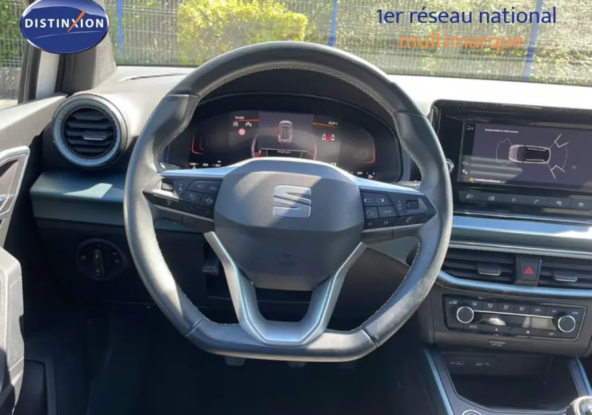 Vue intérieure centrée sur le volant cuir et tableau de bord numérique du SEAT Arona 2025, ambiance noire moderne.