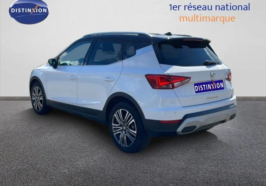 Vue 3/4 arrière droite d’un SEAT Arona blanc avec toit noir et jantes alliage, sur fond neutre intérieur showroom.