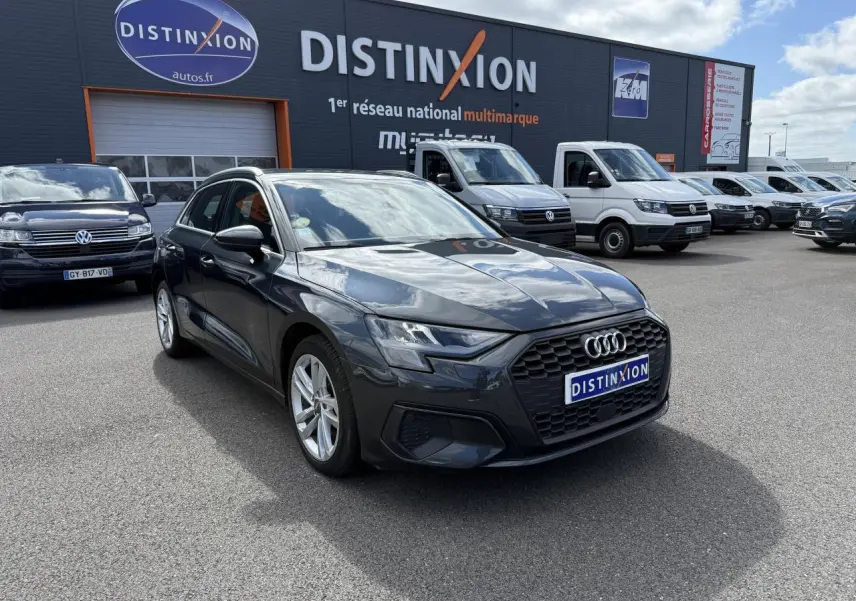 Audi A3 Sportback gris Manhattan métallisé vue 3/4 avant droit sur parking devant concession multimarque Distinxion