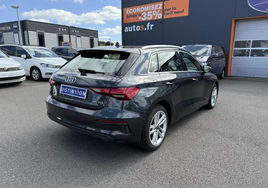 Audi A3 Sportback gris Manhattan métallisé vue 3/4 arrière droit sur parking avec jantes argentées.