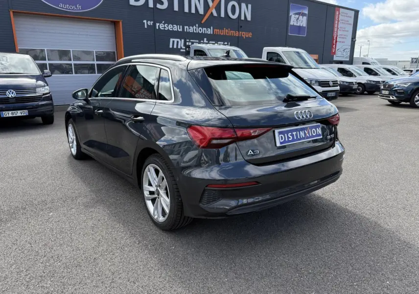 Audi A3 Sportback gris Manhattan métallisé vue 3/4 arrière droit sur parking devant concession multimarque.