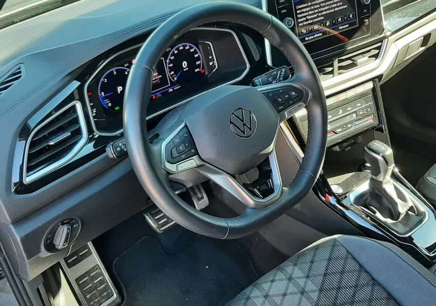Vue intérieure du volant et tableau de bord du Volkswagen T-Roc 2024, avec écran tactile et sellerie tissu gris.
