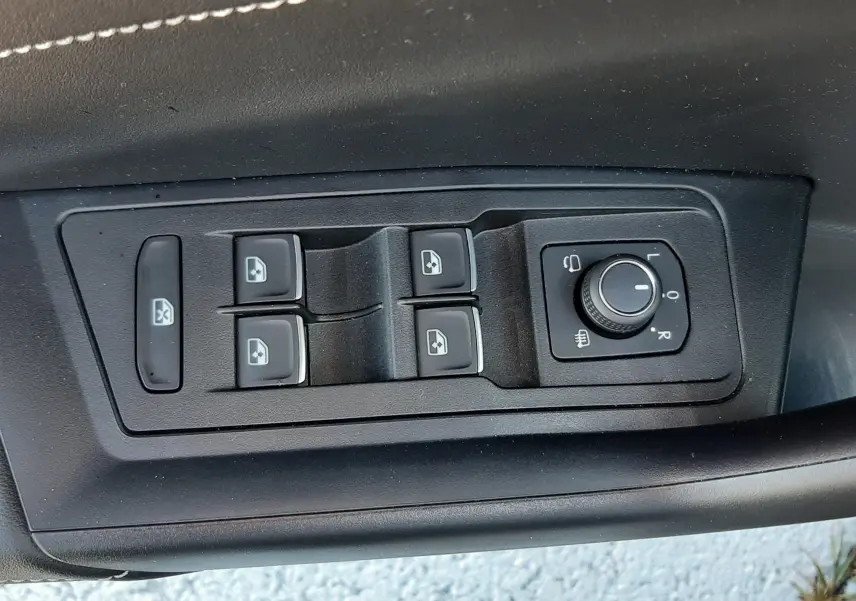 Gros plan sur les commandes de lève-vitres et réglage des rétroviseurs côté conducteur du Volkswagen T-Roc gris Indium 2024.
