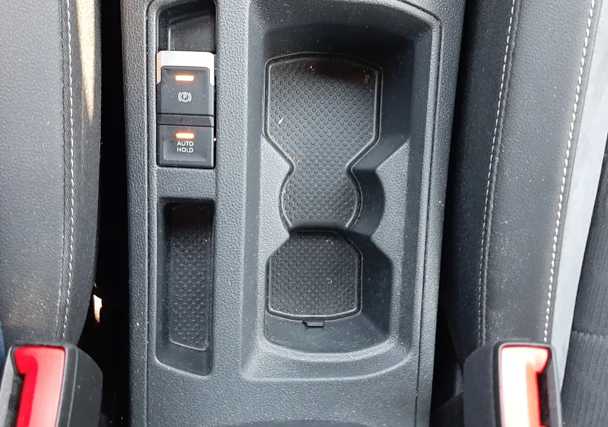 Vue plongeante sur la console centrale noire du Volkswagen T-Roc 2024 avec porte-gobelets et commandes de frein à main électronique.