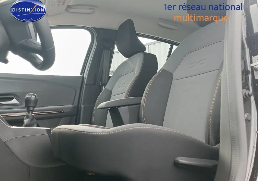 Intérieur avant de la Dacia Sandero noire 2025, vue côté conducteur avec sièges et accoudoir central visibles.