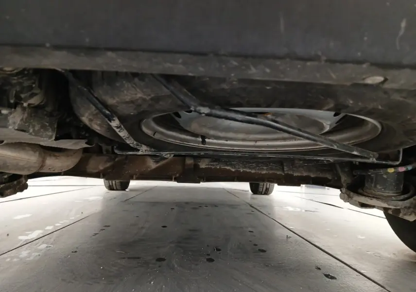 Vue en contre-plongée sous un Renault Kangoo blanc 2024, montrant la roue de secours et le châssis arrière.