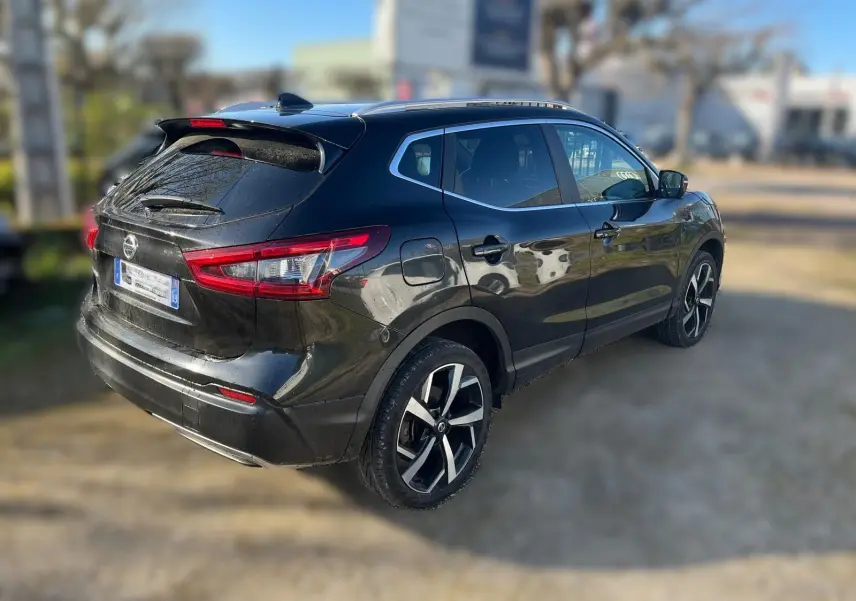 Nissan Qashqai noir en 3/4 arrière droit, avec jantes alu et toit panoramique visible au soleil.
