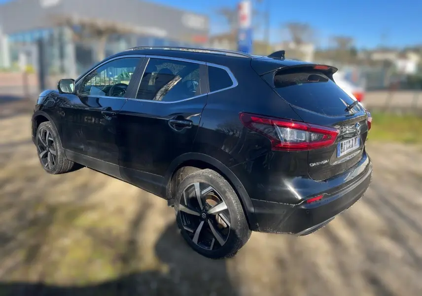 Vue 3/4 arrière droite d'un Nissan Qashqai noir avec jantes alliage et barres de toit visibles.