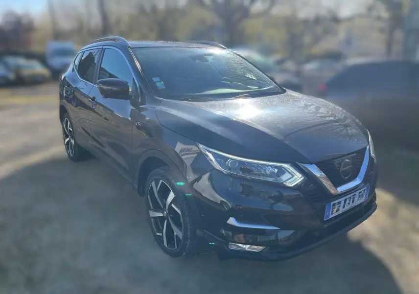 Nissan Qashqai noir en 3/4 avant droit, avec jantes alu et barres de toit visibles au soleil.