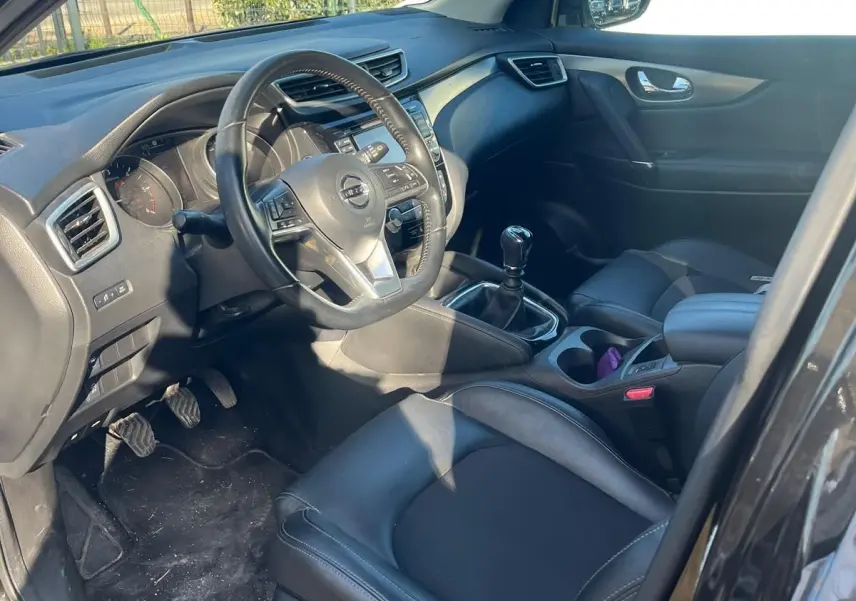 Vue intérieure côté conducteur du Nissan Qashqai noir avec volant cuir multifonctions et boîte manuelle.