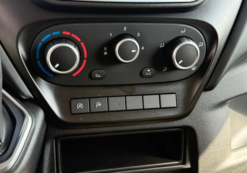 Gros plan sur les commandes de climatisation et boutons fonctionnels du tableau de bord noir de l'Iveco Daily 2.3 blanc.