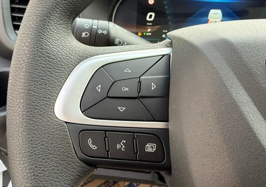 Gros plan sur les commandes au volant du côté gauche du Iveco Daily blanc 2026, avec écran numérique en arrière-plan.