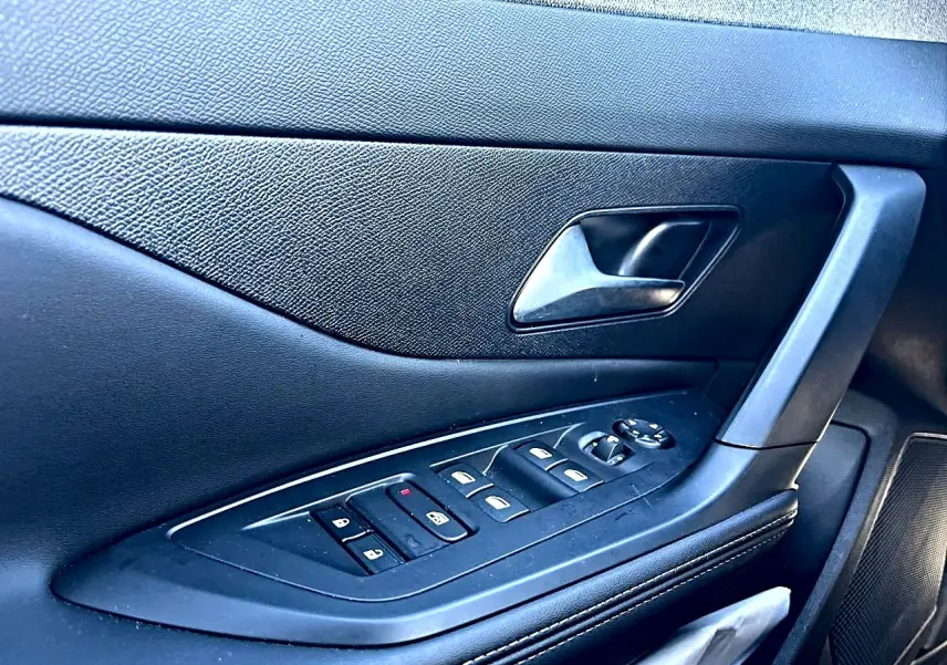 Détail de la porte côté gauche noire avec commandes électriques des vitres et poignée intérieure du Peugeot 308 gris selenium.