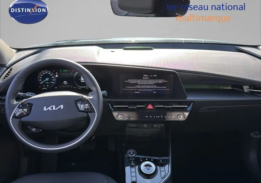 Intérieur moderne du Kia Niro 2025 en vue frontale, tableau de bord noir avec écran tactile et volant multifonction.