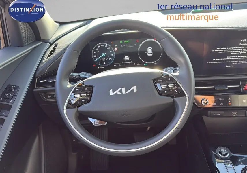 Vue intérieure centrée sur le volant KIA d'un Niro hybride rechargeable 2025 avec tableau de bord numérique et commandes intégrées.
