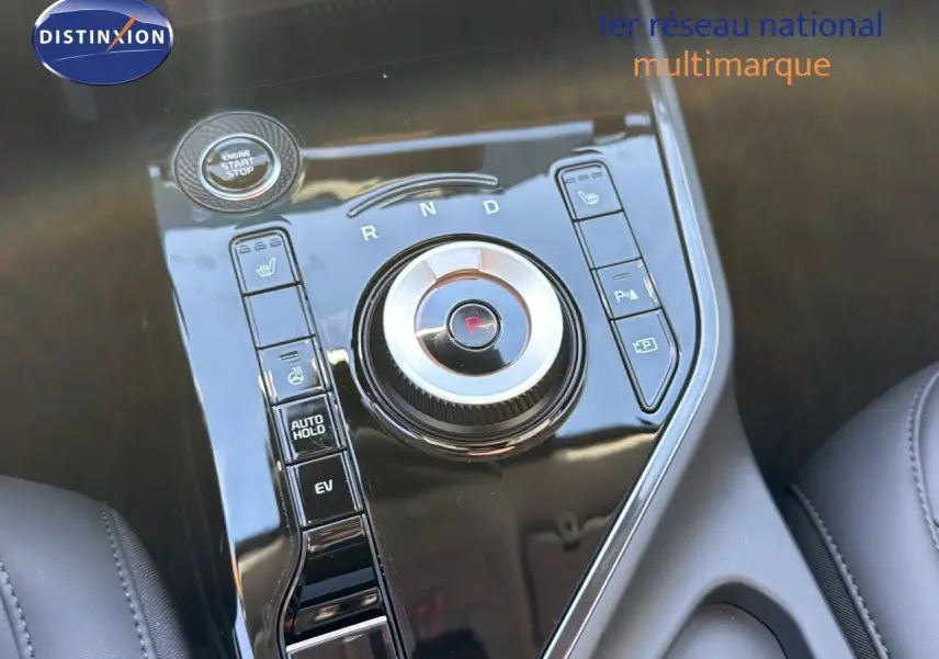 Gros plan sur la console centrale noire brillante du Kia Niro 2025, avec molette de sélection de vitesse et boutons fonctionnels.