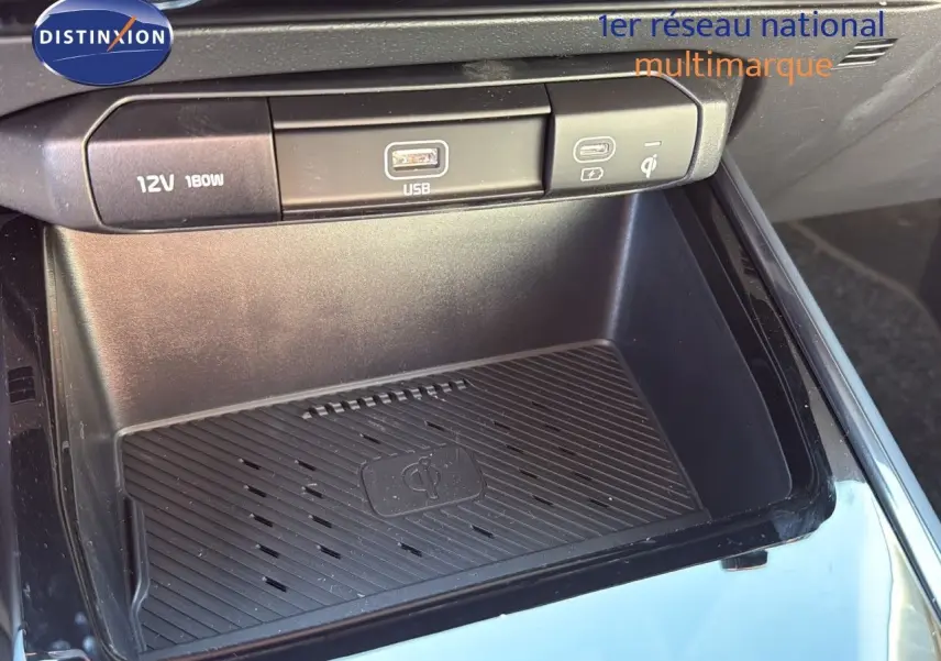 Gros plan sur la console centrale du Kia Niro 2025, avec prise USB, port 12V et chargeur sans fil Qi.