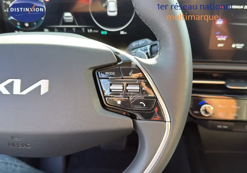 Gros plan sur le côté droit du volant en cuir noir du Kia Niro 2025, avec commandes intégrées et tableau de bord numérique flou.