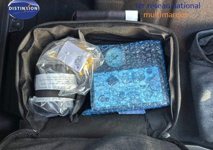 Sac de rangement noir ouvert dans le coffre d'une Kia Niro bleu minéral, contenant des accessoires emballés.