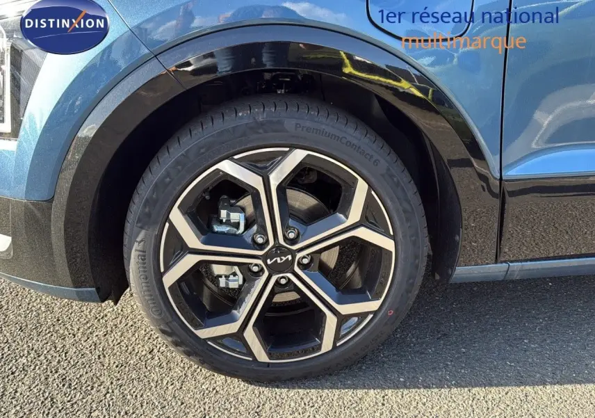 Gros plan sur la roue avant gauche d'un Kia Niro bleu minéral métal 2025 avec jante alliage bicolore.