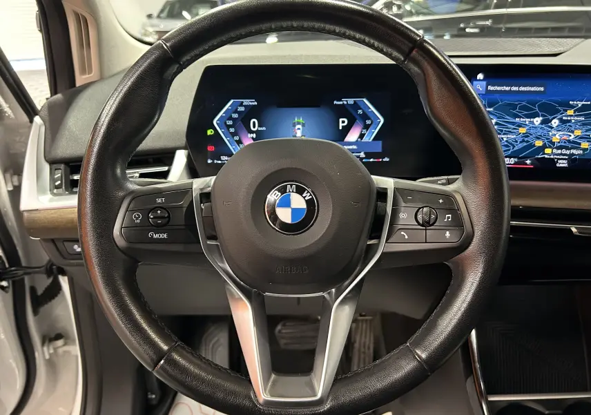 Vue intérieure centrée sur le volant cuir noir de la BMW Série 2 Active Tourer avec tableau de bord digital et écran GPS.
