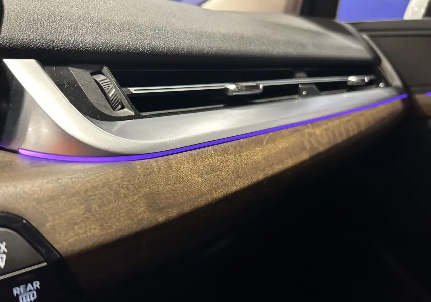 Gros plan sur la planche de bord intérieure avec éclairage d’ambiance violet et finition bois dans une BMW Série 2 Active Tourer.