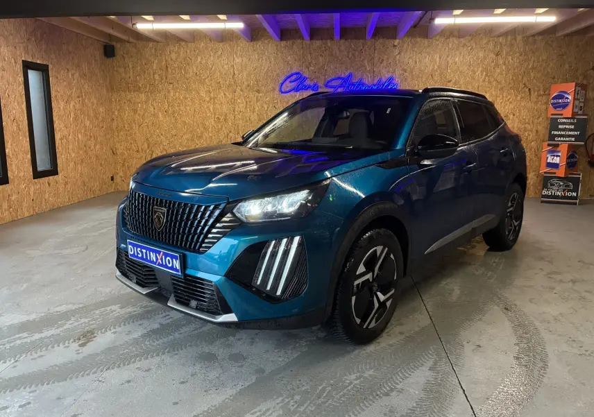 Peugeot 2008 hybride bleu en 3/4 avant droit dans un garage, avec calandre noire et feux LED distinctifs allumés.